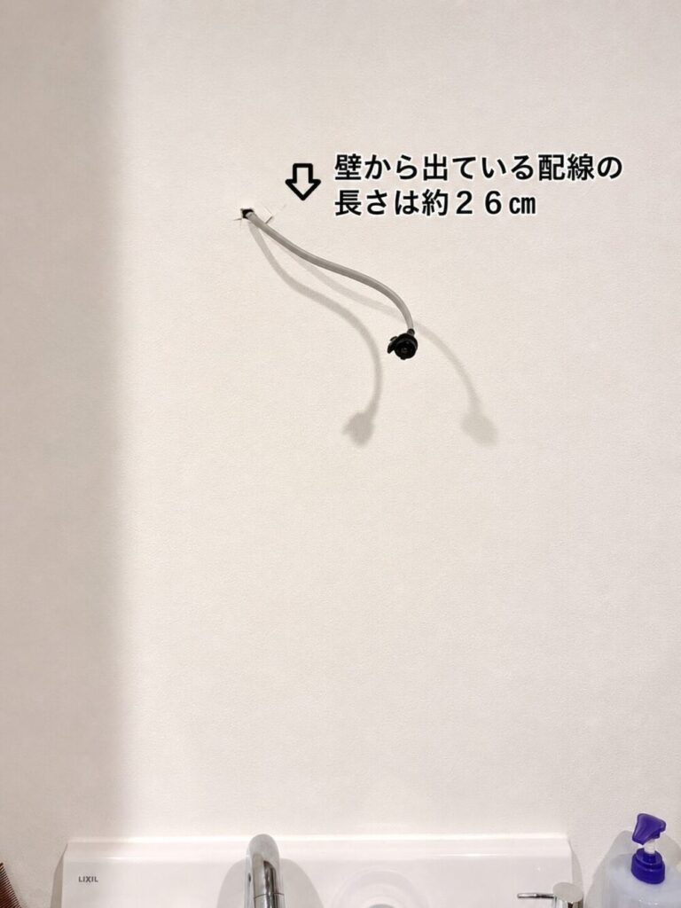洗面室の壁から出ている約26cmの電気配線を確認している写真