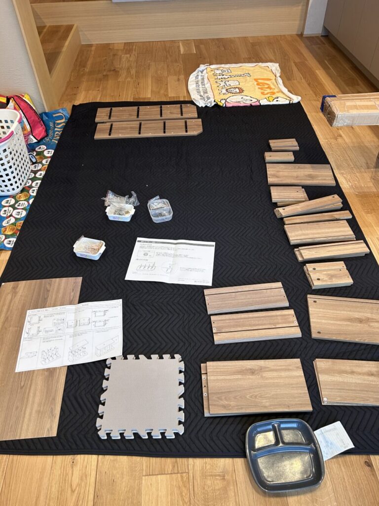 保護マットの上に整理したJKプラン木製ローチェストの部品と説明書